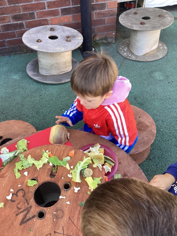 A child sitting in the outdoor kitchen playing with some vegetables on the table