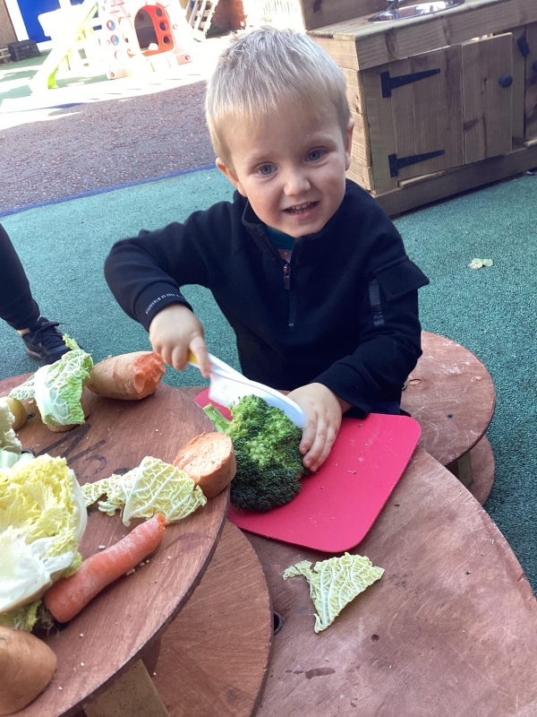 A child chopping up some broccoli at a table in the outdoor kitchen