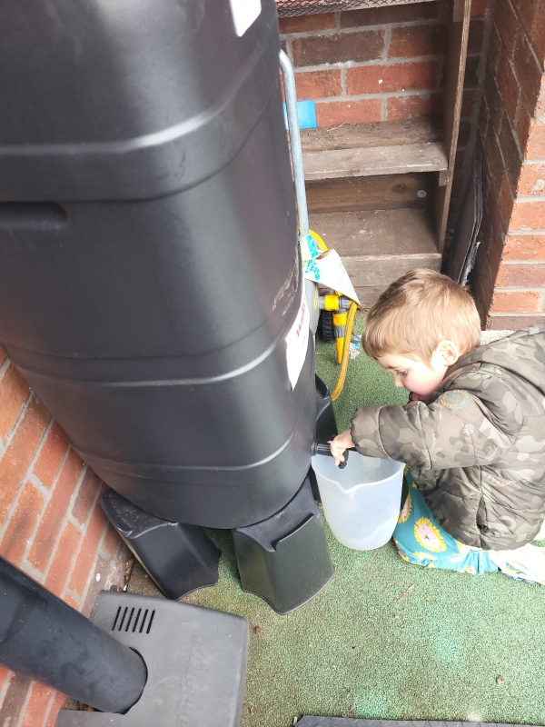 A child fills up a jug from the rainwater collection barrel