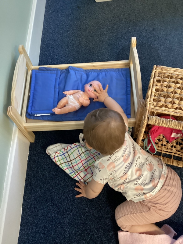 A toddler plays with a doll in a cot